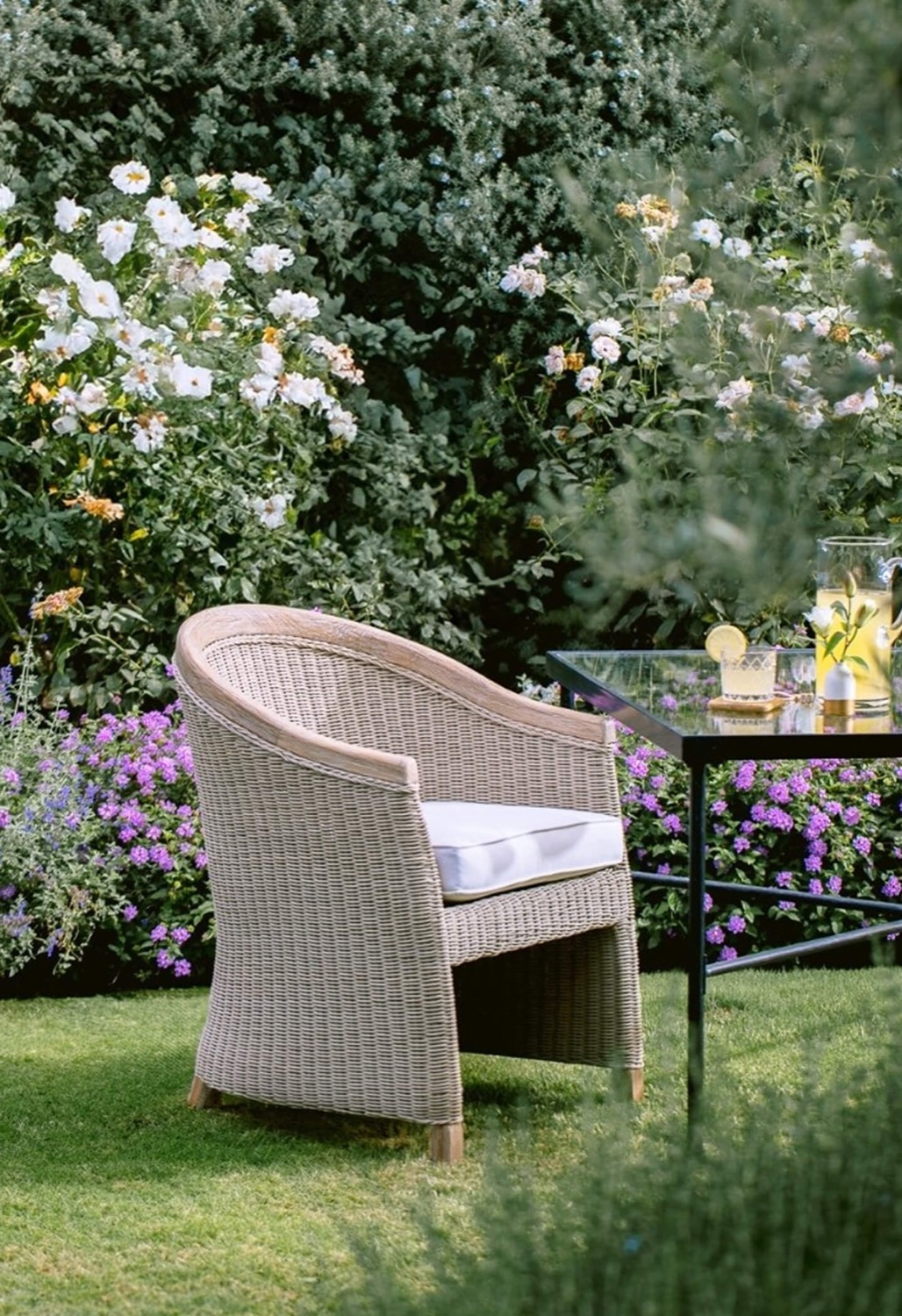 Woven tub chair and glass table in a flowering garden
