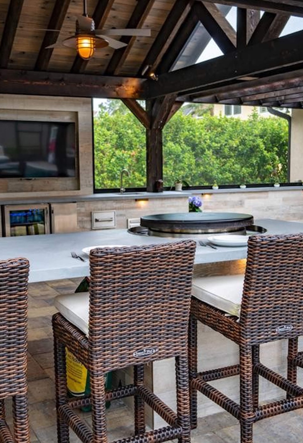 Covered outdoor kitchen with woven bar stools under a glowing pendant lamp