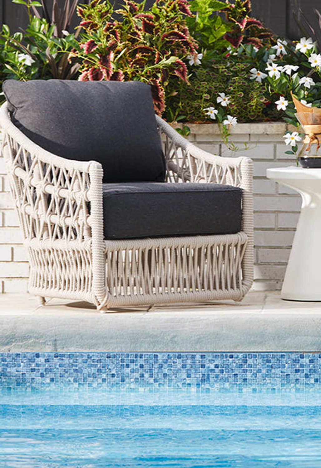 White rope-weave lounge chair with charcoal cushions at the edge of a pool
